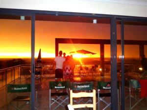 um grupo de pessoas olhando para o pôr do sol através de uma janela em Rio Manso Apartamentos em Victoria