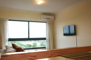 1 dormitorio con ventana grande y TV en la pared en Rio Manso Apartamentos en Victoria