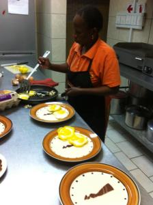 a woman standing in a kitchen with plates of food at Normann Safari Bush Lodge in Phalaborwa