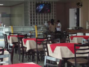 two people standing in a restaurant with tables and chairs at Marinho Plaza Hotel in Capellinha
