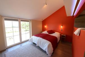 1 dormitorio con pared de color naranja, cama y ventana en Les Coteaux du Vinave, en Herve