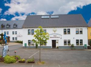 un edificio blanco con un árbol en un estacionamiento en Landgasthof zum Siebenbachtal en Strotzbüsch