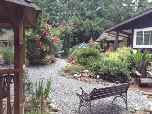 a bench in a garden with flowers and plants at Tea Cozy Bed & Breakfast in Qualicum Beach