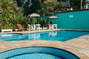 a swimming pool with chairs and tables and umbrellas at Arco Iris Chales II in Maresias