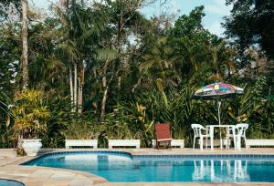 a swimming pool with a table and an umbrella at Arco Iris Chales II in Maresias