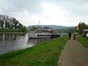 a boat on a river with people walking on a sidewalk at Ferienwohnung Mebes in Polle