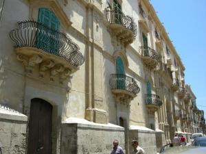2 personas caminando frente a un edificio con balcones en Affittacamere Conte Di Cavour, en Noto