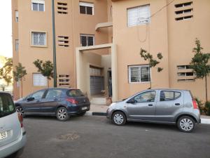 due auto parcheggiate in un parcheggio di fronte a un edificio di Appartement Bader a Marrakech