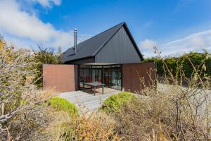 una pequeña casa con techo negro en una playa en The Black House with Stunning Outdoor Bath, en Lake Tekapo