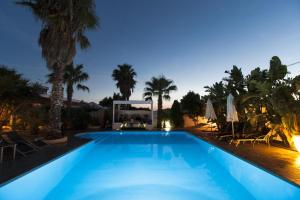 a blue swimming pool with palm trees and umbrellas at tenuta cotriero in Marina di Mancaversa