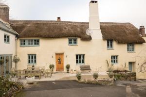 een oud huis met een rieten dak en banken bij Glebe Farm B&B in Kingsbridge