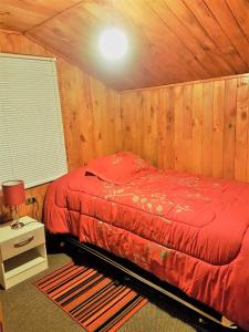 a bedroom with a red bed in a wooden room at Cabañas Emma in Osorno