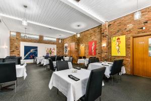 un restaurante con mesas y sillas blancas y una pared de ladrillo en William Macintosh Motor Lodge, en Naracoorte