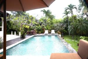 a swimming pool with two chairs and an umbrella at Urbanest Inn Villa in Seminyak