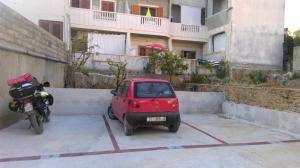 una piccola auto parcheggiata accanto a una moto in un parcheggio di Guest House Marija a Sumartin