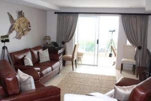 sala de estar con muebles de cuero marrón y puerta corredera de cristal en Seafront Apartment in Mossel Bay en Mossel Bay