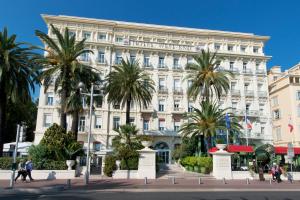 a large white building with palm trees in front of it at Hôtel West End Promenade in Nice