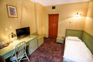 a room with a bed and a desk with a television at Hotel Calisia in Kalisz