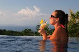a woman drinking a drink in a swimming pool at Puri Mangga Sea View Resort and Spa in Lovina
