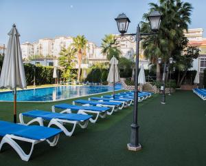 eine Reihe von Liegestühlen und Sonnenschirmen neben einem Pool in der Unterkunft Apartamentos Mediterráneo Real in Fuengirola