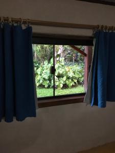 ein Fenster mit blauen Vorhängen in einem Zimmer in der Unterkunft Suíte Cravo & Canela in São Pedro da Serra