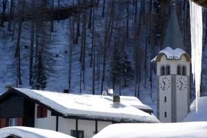 een gebouw met een klokkentoren in de sneeuw bij Haus Alpenperle in Saas-Almagell