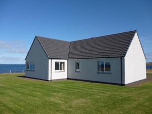 a house on a field with the ocean in the background at Mey Cliff Cottage in Scarfskerry