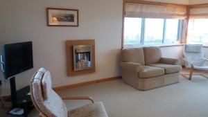 sala de estar con sofá, silla y TV en Mey Cliff Cottage, en Scarfskerry