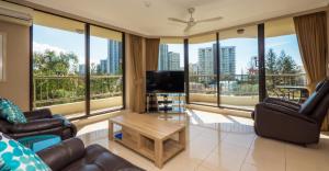 a living room with a couch and a tv and large windows at Aristocrat Apartments in Gold Coast