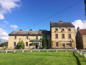 Worsley Arms Hotel في Hovingham: مبنى من الطوب كبير مع حديقة خضراء أمامه