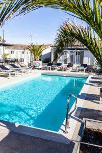 a swimming pool with blue water and palm trees at Hotel Les Bois Flottais in Le Bois-Plage-en-Ré