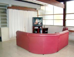 a red couch in a living room with a tv at Hotel Ximenes in Casimiro de Abreu