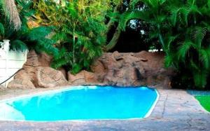 a blue swimming pool in front of some trees at Rustenburg Boutique Hotel in Rustenburg