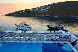 a pool with chairs and boats in the water at Petasos Beach Resort & Spa - Small Luxury Hotels of the World in Platis Gialos
