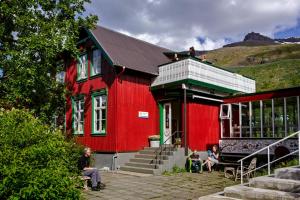 un edificio rosso con persone sedute fuori di Hafaldan HI hostel, old hospital building a Seyðisfjörður