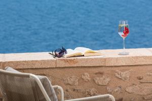 a glass of wine and a book on a wall with a drink at Moni Emvasis Luxury Suites in Monemvasia