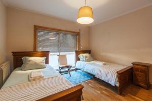 two beds in a room with a chair and a window at Sea You Espinho in São Félix da Marinha