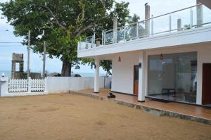 a white building with a balcony and a tree at Blue Wings Beach Hotel in Trincomalee
