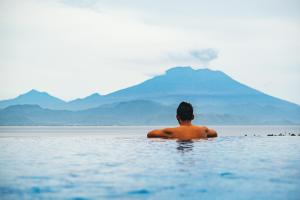 a man in the water with a mountain in the background at Jenggala Hill in Nusa Lembongan