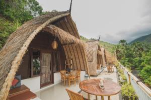 Casa con techo de paja, mesa y sillas en Amed Paradise Warung & House Bali, en Amed