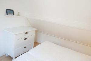 - une chambre blanche avec un lit et une commode blanche dans l'établissement Egmondaanzeevakantiehuisje, à Egmond aan Zee