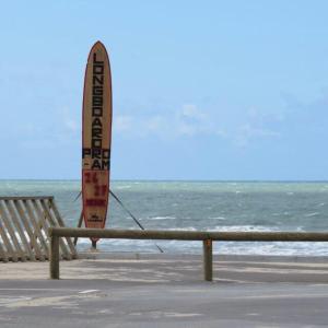 une planche de surf assise sur la plage à côté d'un banc dans l'établissement La maison d'été de mes parents, à Vendays-Montalivet