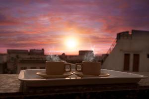 two coffee cups sitting on a plate on a balcony with a sunset at Hotel Sanmukh By Adamo in Nāthdwāra