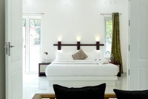 a white bedroom with a large white bed and windows at Bamboo Creak in Thekkady