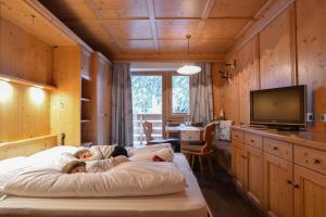 eine Familie auf einem Bett in einem Zimmer mit einem TV in der Unterkunft Residence Ciasa Vedla in Abtei