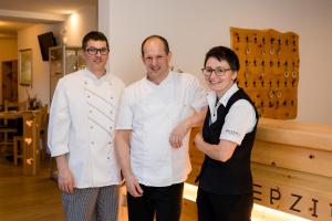 three men standing next to each other in a kitchen at Hotel Helvetia in Müstair