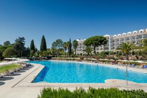 a large swimming pool with chairs and a hotel in the background at Penina Hotel & Golf Resort in Portimão