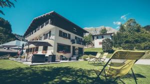 - un bâtiment avec des chaises et un parasol dans une cour dans l'établissement Hôtel Flor'Alpes, à La Giettaz