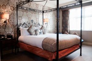 1 dormitorio con cama con dosel y papel pintado con motivos florales en The White Hart Hotel en Kingston upon Thames