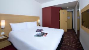 a hotel room with a large white bed with a magazine on it at ibis Seef Manama in Manama